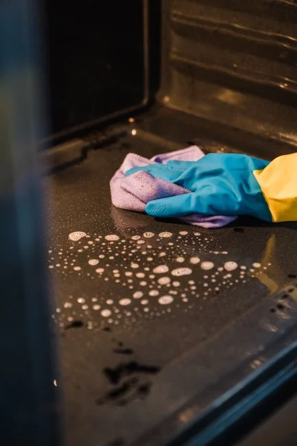 Jeune femme équipée de gants en caoutchouc tenant une bouteille avec le logo recyclage à l’intérieur, mettant en avant un nettoyage respectueux de l’environnement.